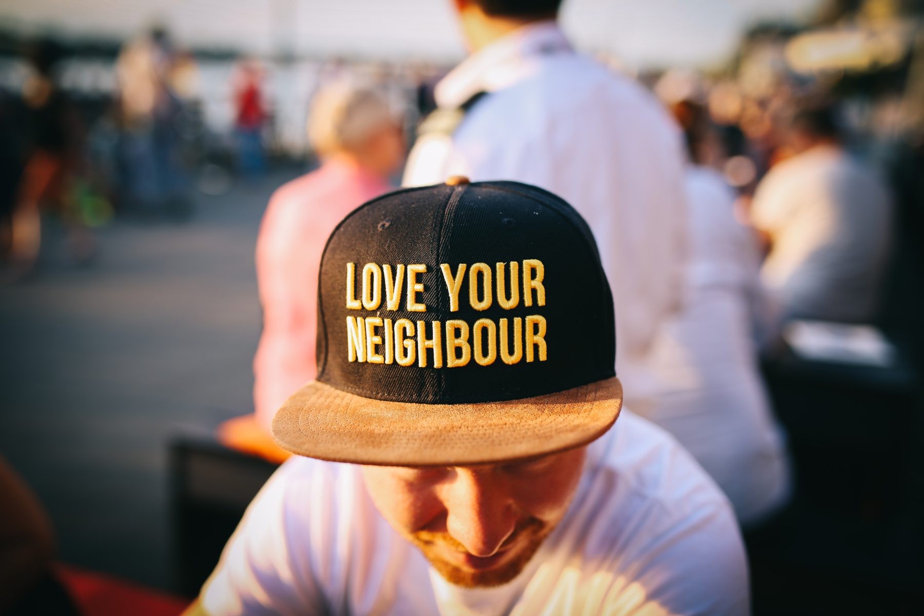Mann in einer Menschenmenge trägt eine Kappe mit der Aufschrift „Love Your Neighbour“.